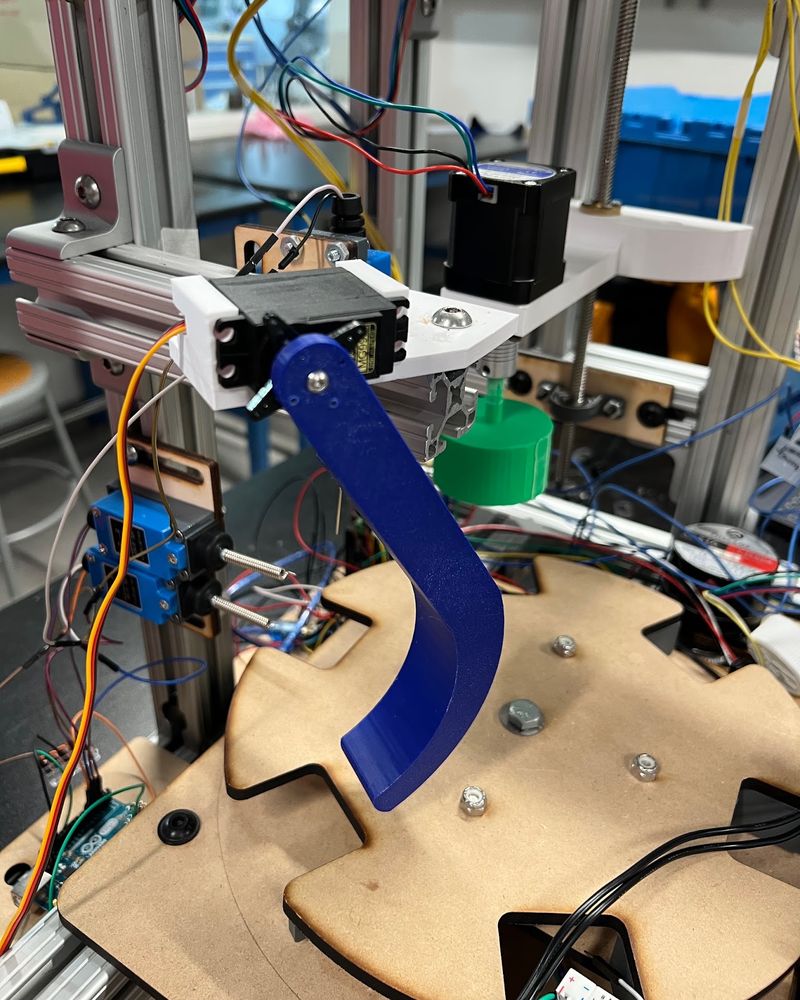 The rejection station: a servo on a white bracket drives the curved blue rejector arm over the rotary table, with a blue whisker switch beside it
